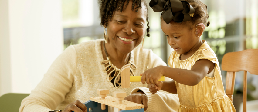 A woman smiling while watching a toddler play with toys